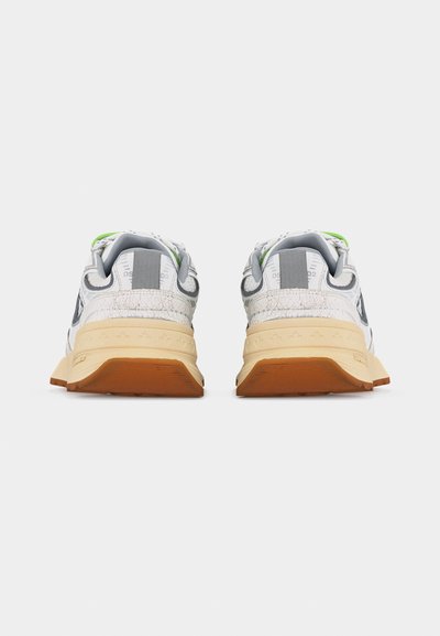 Paire de baskets blanches avec semelles beige vues de dos, présentant des accents gris et verts ainsi que des détails texturés sur le talon.