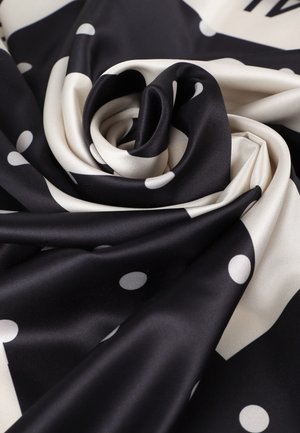 Black and cream silk fabric, featuring large white polka dots, arranged in a spiral pattern, highlighting its smooth, glossy texture.