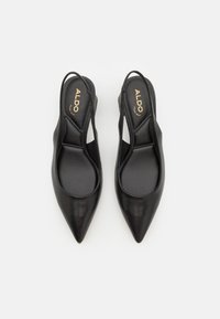 Bottines noires en cuir avec bouts pointus, côtés découpés et une texture lisse, affichant un logo sur les semelles intérieures.