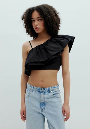 Zwarte crop top met één schouder en een gerimpeld ontwerp, gemaakt van een gladde stof. Gecombineerd met een lichtblauwe high-waisted denim jeans.