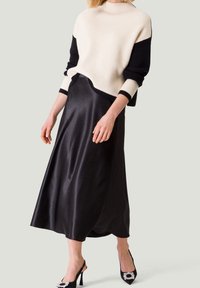 Pull en tricot crème et noir, coupe décontractée ; jupe noire en satin, longueur chevilles ; escarpins noirs ouverts avec embellissements.