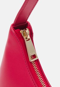 Sac en cuir rouge avec une texture lisse, doté d'un détail de fermeture éclair dorée, mettant en valeur la tirette en métal et la doublure en tissu à l'intérieur.