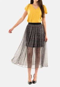 Jupe maxi noire fluide avec superposition en voile texturé ; taille extensible. Associée à un haut à manches courtes et décolleté en V couleur moutarde.