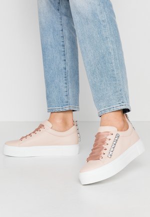 Lichtroze sneakers met brede satijnen veters en strass-steentjes, gedragen met lichtblauwe cropped jeans op een neutrale achtergrond.