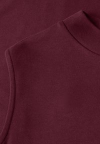 Gros plan sur un tissu bordeaux montrant le col et la couture de l'épaule d'un vêtement à manches longues, mettant en valeur la texture et les détails de la couture.