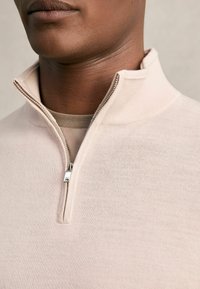 Hellbeige Quarter-Zip-Pullover aus strukturiertem Stoff, ausgestattet mit einem silbernen Reißverschluss und einem schlichten, minimalistischen Design.