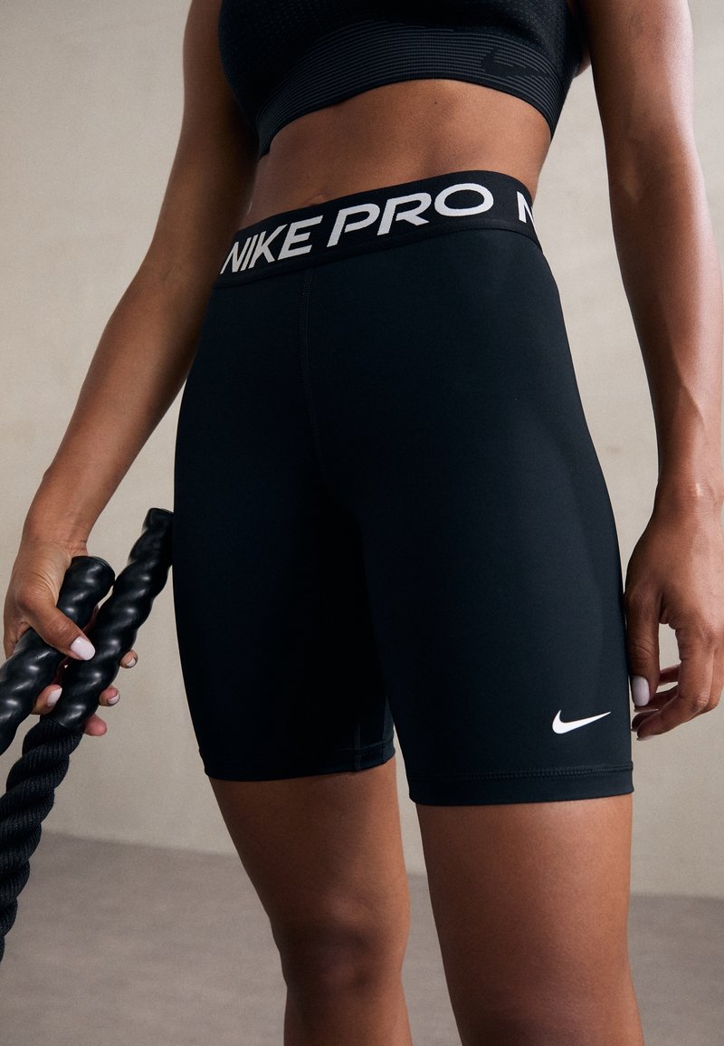 Shorts Nike Pro noirs avec un logo blanc sur la jambe inférieure. La ceinture porte le texte « NIKE PRO » en blanc sur fond noir.