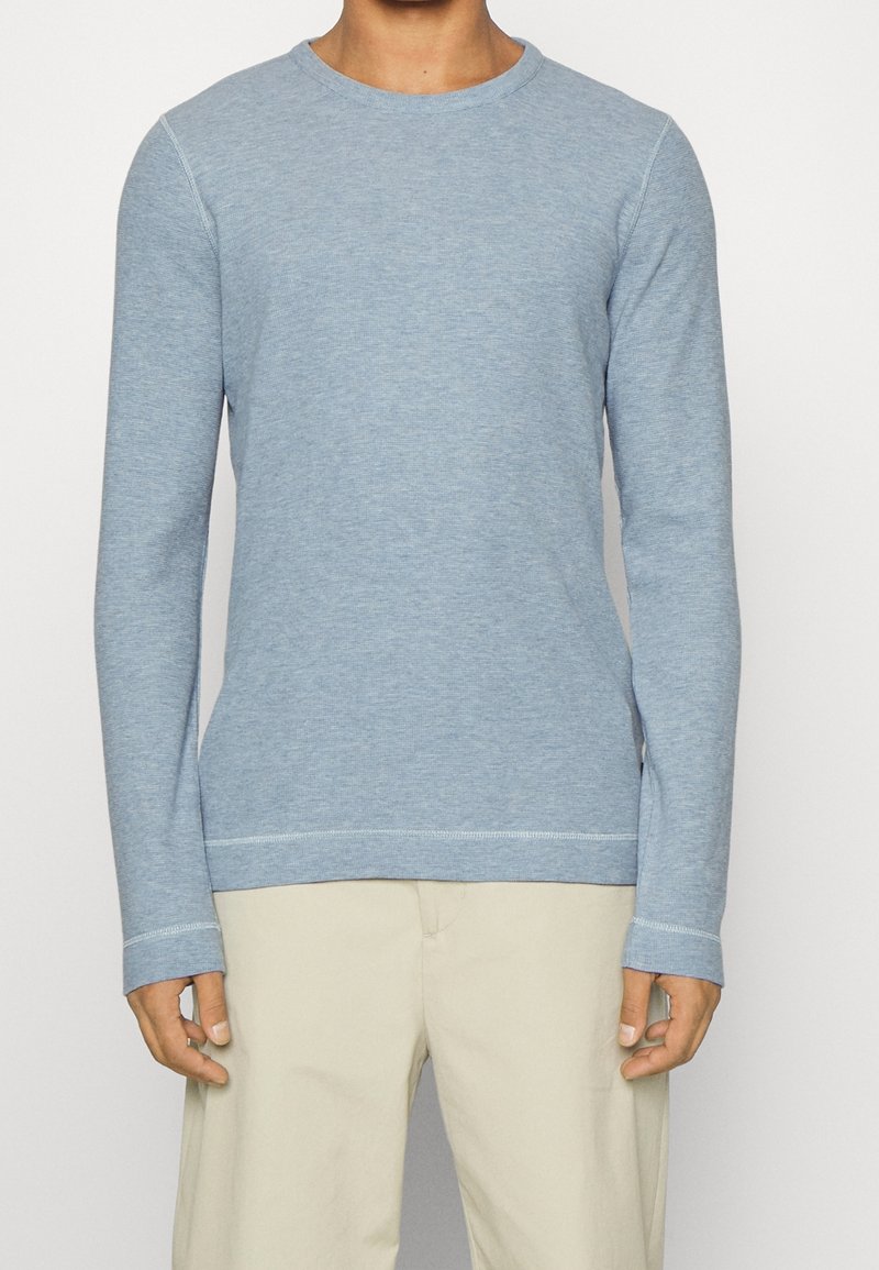 Ljust blå långärmad tröja med rund hals i ett mjukt, texturerat tyg som har ribbade ärmslut och nederkant. Tröjan har en minimalistisk design.