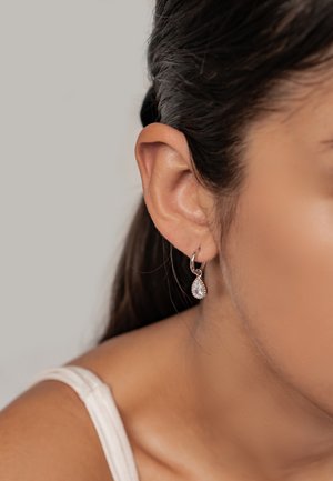 Silberne Creolen mit einem hängenden, tropfenförmigen Kristall, mit einer polierten Oberfläche und glattem Texture.