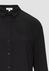 Zwarte button-up shirt met een gestructureerde stof, voorzien van een kraag en knopen aan de voorkant, ontworpen voor een losse pasvorm. Merklabel zichtbaar aan de binnenkant.