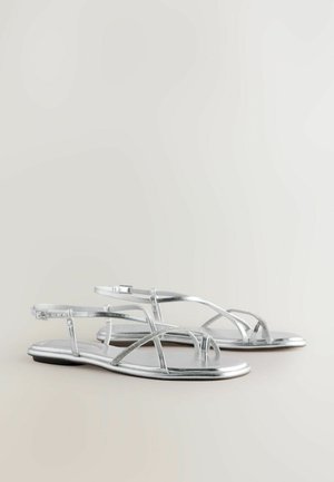 Silberne flache Sandalen mit einem Riemen design, ausgestattet mit metallischen Riemen und einer glatten Textur. Offene Zehen und ein minimalistischer Stil sind bemerkenswerte Details.