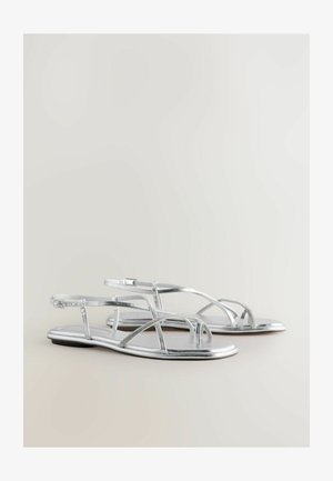 Des sandales plates argentées avec un design à lanières, présentant des lanières métalliques et une texture lisse. Les orteils ouverts et le style minimaliste sont des détails notables.