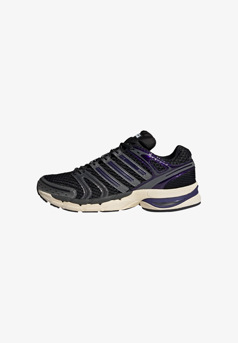 Chaussure de course basse noire et violette avec tige en mesh, renforts en plastique, semelle beige amortie et semelle extérieure texturée.