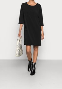 Vestido negro con mangas 3/4, escote redondo y corte recto. Llevado con botines negros hasta el tobillo y un bolso blanco de estampado de serpiente.