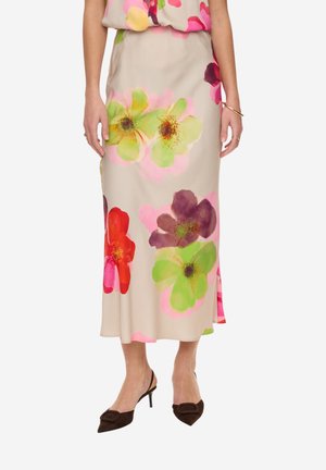 Jupe midi beige avec de grands imprimés floraux colorés en vert, rouge, violet et rose, portée avec des escarpins à bout pointu marron foncé.
