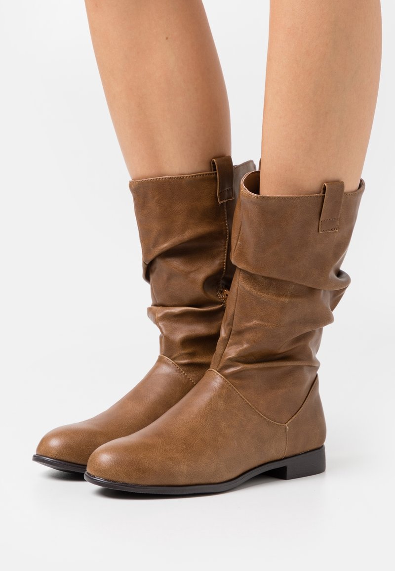 Bottes cheville en similicuir marron à design décontracté, bout arrondi, semelle plate et languettes sur le dessus pour faciliter l'enfilage.