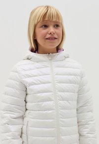 Doudoune blanche avec un motif matelassé horizontal, équipée d'une fermeture éclair à l'avant et d'une capuche. La doublure intérieure est de couleur violet clair.