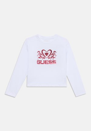 T-shirt court à manches longues blanc avec un motif de cœur rouge avec des tourbillons et le logo "GUESS" en lettres majuscules. Matière en coton doux.