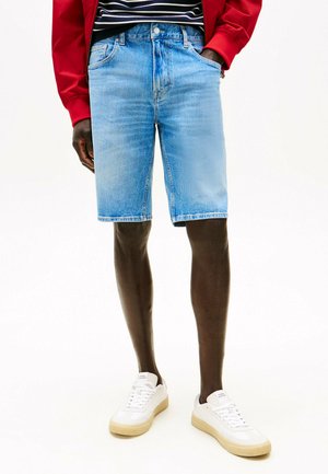 Lichtblauwe denim shorts met een klassiek ontwerp, voorzakken en omgeslagen randen, gecombineerd met witte sneakers. Rood jasje eroverheen.