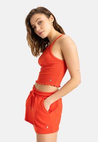 Roter gerippter Croptop mit gewelltem Saum und seitlichem Logo, kombiniert mit roten Shorts mit Kordelzug und seitlichen Taschen. Glattes, dehnbares Material.