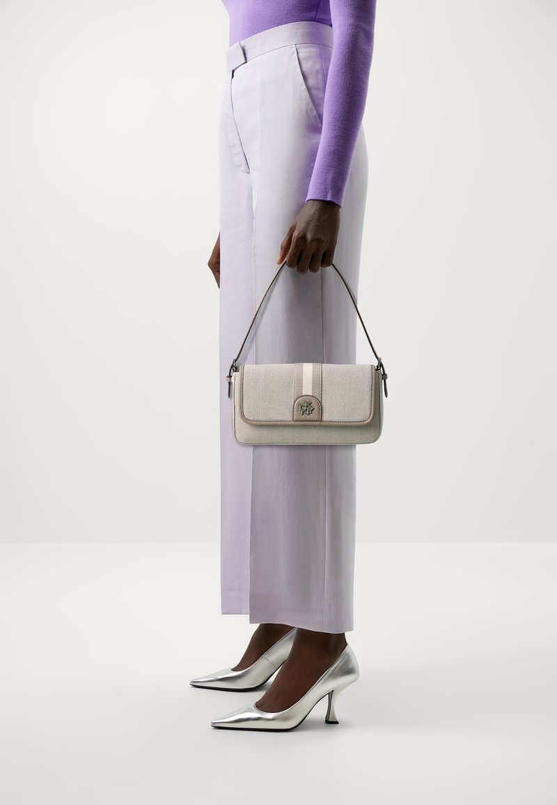 Beige textured handbag with a flap, silver hardware, and a strap. Worn with light lilac wide-leg trousers and silver heels.