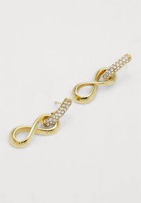 Boucles d'oreilles en or en forme de symboles infinis, avec une finition lisse et une section ornée de strass clairs.