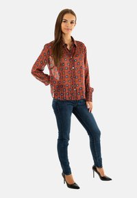 Camisa de botones de patrón rojo y azul con un ajuste relajado, combinada con jeans skinny azul oscuro y tacones altos negros.