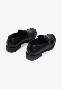 Zapatos de cuero negro sin cordones con un tacón bajo y rectangular y punta redondeada. Presentan una textura suave y un detalle de costura simple.