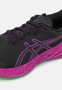 Zapato deportivo negro con acentos morados y detalles reflectantes. Presenta una parte superior texturizada, cordones redondos y una entresuela moteada de colores.