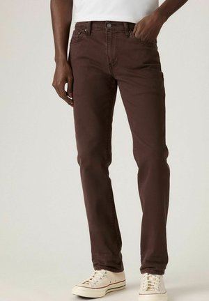 Brown cotton jeans with a straight leg design, featuring front pockets and a button closure, paired with white sneakers.