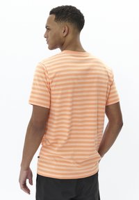 Striped t-shirt in light orange with thin horizontal lines, soft texture, crew neck, and a label visible near the hem.