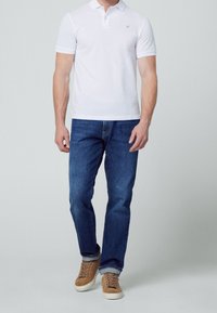 Polo blanc, manches courtes, col classique ; associé à un jean bleu foncé et des sneakers en suédine beige avec des semelles crème. Design simple, sans motifs.