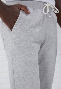 Pantalones de chándal grises con una textura suave, cinturilla elástica con cordón y bolsillos laterales. Una vista en primer plano de la cinturilla y el detalle del bolsillo.