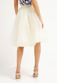 Tulle skirt in cream, knee-length, with a fitted waistband and layered design. Paired with light pink high-heeled sandals.