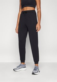 Sorte joggebukser med elastisk midje og snor. Fittede mansjetter ved anklerne. Kombinert med grå treningssko med strukturert design.