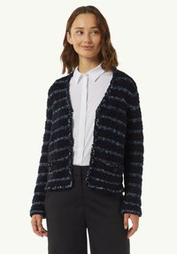 Texturiertes cardigan in Marineblau und Blau mit Streifen, locker geschnitten, offenes Frontdesign und zwei Knöpfen, kombiniert mit einem weißen Hemd und schwarzen Hosen.