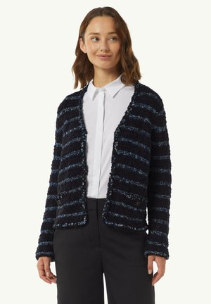 Texturiertes cardigan in Marineblau und Blau mit Streifen, locker geschnitten, offenes Frontdesign und zwei Knöpfen, kombiniert mit einem weißen Hemd und schwarzen Hosen.