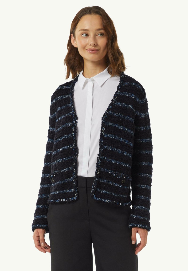 Texturiertes cardigan in Marineblau und Blau mit Streifen, locker geschnitten, offenes Frontdesign und zwei Knöpfen, kombiniert mit einem weißen Hemd und schwarzen Hosen.