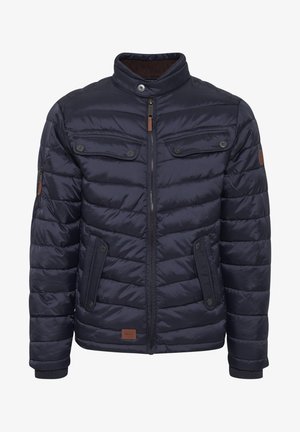 Sötétkék puffos kabát álló gallérral, cipzáras záródással, két mellzsebbe kis fedővel és kontrasztos barna részletekkel a galléron és a címkén.