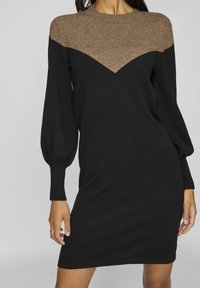 Robe noire avec de longues manches bouffantes et un empiècement texturé marron, présentant un motif en chevrons. Matériau doux et tricoté. Forme simple et ajustée.