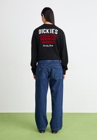 Black sweater with white and red text on the back, paired with dark blue wide-leg denim jeans. Simple design and relaxed fit.