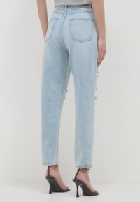Jean en denim bleu clair taille haute avec une coupe droite, présentant des accents déchirés sur les côtés et des poches à rabat à l'arrière.