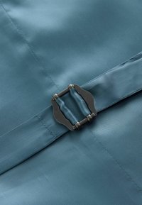 Ceinture en tissu bleu avec boucle en métal noir serrée sur un fond textile bleu assorti.