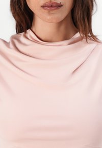 Světle růžový top s véčkovým výstřihem vyrobený z hladké, elastické látky. Disponuje jemným řasením kolem výstřihu a přiléhavým siluetou.