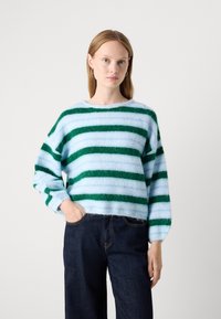 Gestreepte trui in zachte, donzige blauw- en groentinten; ruime pasvorm, ronde hals en lange mouwen gecombineerd met donkere spijkerbroek.