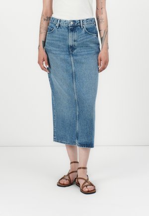 Lys blå denim midi-skjørt med rett snitt, fem lommer og synlige sømmer. Kombinert med brune spissede sandaler.