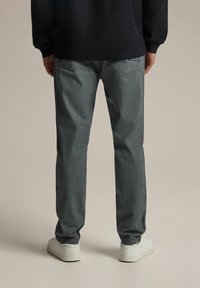 Męskie szare dżinsy o subtelnej fakturze, prostym kroju i dużych tylnych kieszeniach. W połączeniu z białymi trampkami.