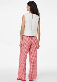 Top bianco senza maniche con apertura a chiave sul retro, abbinato a pantaloni rossi in gingham a gamba larga. L'outfit presenta una vestibilità comoda e un tessuto texturizzato.