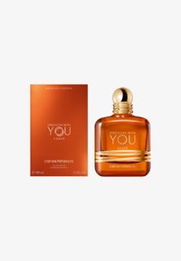 Bursztynowa szklana butelka z złotymi akcentami, z zaokrągloną zakrętką. W zestawie pomarańczowe pudełko z napisem "Stronger With You Amber." 100 ml.