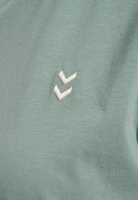 Tissu vert clair avec deux petites formes de chevrons blancs brodées très proches l'une de l'autre à la surface.